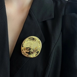 Minimalist irregular gold round brooch with textured surface on black suit lapel