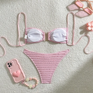 Flat lay of smocked light pink bikini with a gold U-buckle on white faux fur