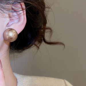 Close-up of elegant large golden spherical stud earrings worn by a model in soft lighting