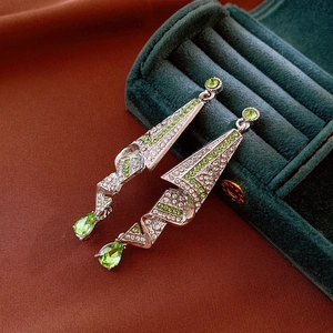 Macro detail of geometric silver earrings with green water drop zircon on velvet