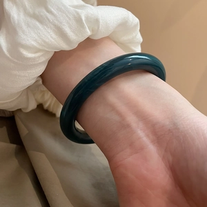 Close-up of deep green resin open cuff bracelet worn with elegant pleated white sleeve