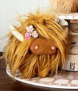 Macro shot of Highland Cow plush with long brown fur, white horns and pink flower detail