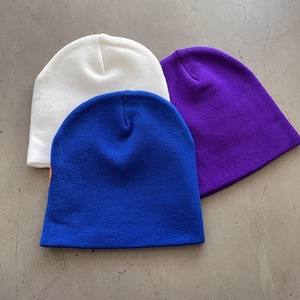 Close-up of white, purple, and royal blue knitted beanies with fine ribbed texture