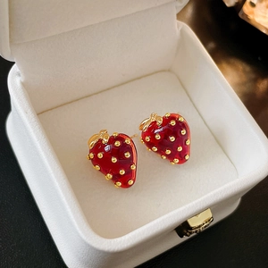 Close-up of red strawberry stud earrings with golden leaf details on a white jewelry pad