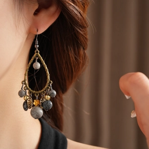 Detail of drop-shaped vintage bronze earrings with grey beads and golden floral accents
