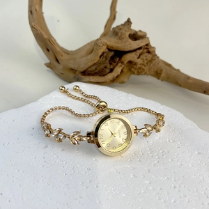Detail of gold quartz bracelet watch with leaf-shaped stones on textured stone surface