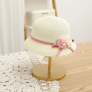 Detail of a cream woven straw hat featuring pink fabric roses and delicate lace leaves