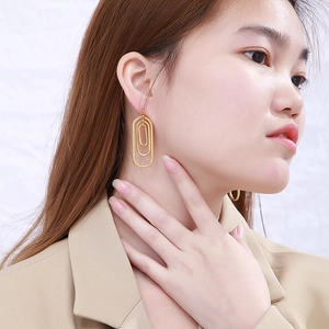 Close-up of golden multi-layer oval geometric earrings worn by a model for scale
