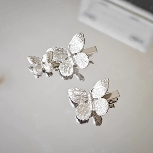 Detailed macro view of silver butterfly hair clips with metallic texture on a mirror surface