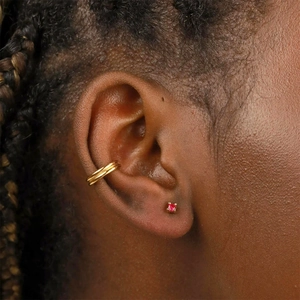 Gros plan sur un ear cuff doré à double anneau et une puce d'oreille en rubis rond