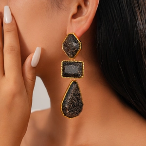 Détail de boucles d'oreilles géométriques en résine avec cadres dorés et pierres noires