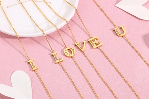 Detail of gold letter bracelets I-L-O-V-E-U with shimmering crystal pavé in pink background