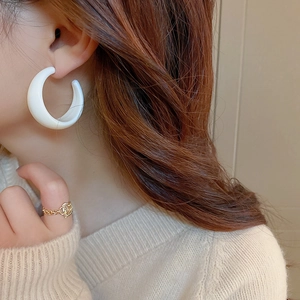 Close-up of a model wearing a white C-shaped resin earring and a gold chain ring