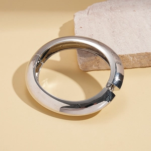 Detailed view of polished silver metal bangle with a hinged clasp on stone background