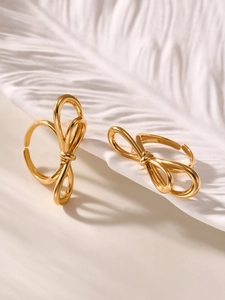 Close-up of polished 18k gold-plated bow rings on a minimalist textured background