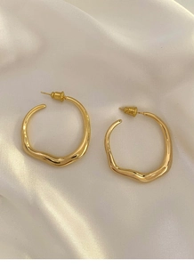 Close-up of gold irregular round hoop earrings on soft white silk fabric background