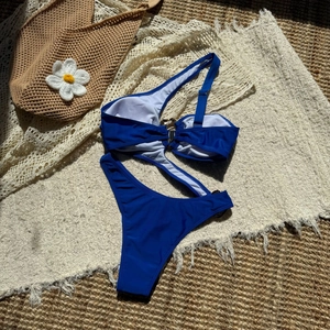 Detail of royal blue asymmetric monokini with side cut-outs and golden ring hardware