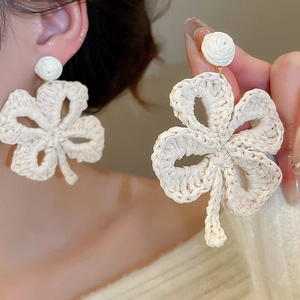 Macro detail of bohemian cream raffia woven flower earrings with high texture and craftsmanship