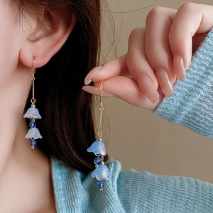 Elegant gold lily of the valley tassel earrings with blue petals on model ear