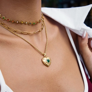 Layered gold necklaces featuring a green heart gemstone pendant and colorful beads on a model