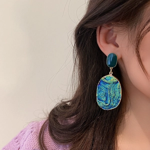 Close-up of heart-shaped blue resin earrings with golden metal edges on model
