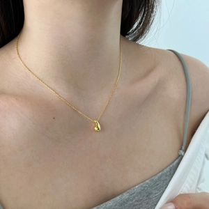 Detail of a minimalist gold teardrop pendant necklace worn on a model's neck