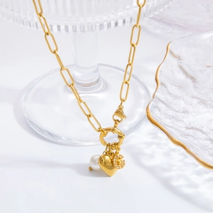 Detail of gold paperclip chain necklace with pearl, heart pendant, and G-shaped charm