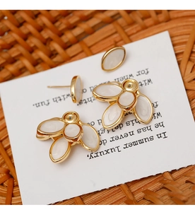 Detail of French vintage gold earrings with white petals on a woven basket background