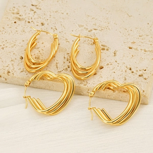 Minimalist layered gold heart and oval earrings on travertine and silk background