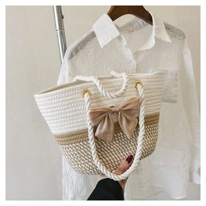 Detail view of woven tote bag with a khaki fabric bow and white rope handle straps