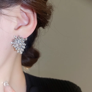 Detail shot of sparkling silver leaf-shaped earrings with crystals on female model ear