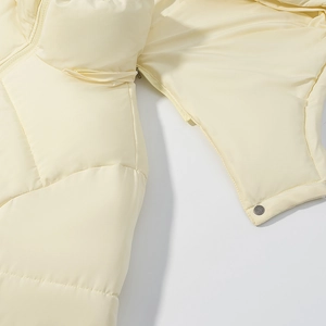 Detail of cream quilted puffer jacket showing smooth fabric, zipper, and metal button