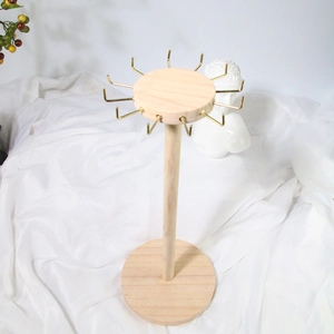 Rotating wooden jewelry display stand with gold hooks on a minimalist white background