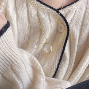 Detail of a gold oval shell pendant necklace paired with a beige cable-knit cardigan