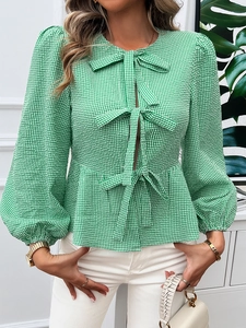 Detail of green plaid blouse with puffy sleeves, bow tie, and ruffled hem on female model
