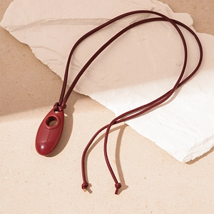 Deep red resin pebble pendant necklace with hollow design on white stone background