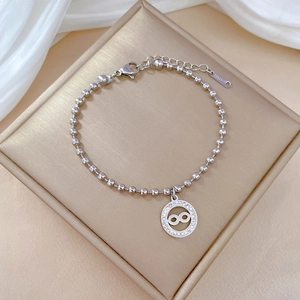Macro detail of silver stainless steel infinity charm bracelet on white silk padding