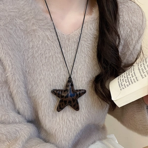 Detailed close-up of a leopard print star pendant necklace worn on a beige knit sweater