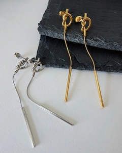 Detail of gold and silver knot drop earrings with snake chains on grey stone