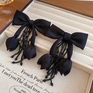 Detail of elegant black fabric bow earrings with crystal floral tassels on a beige tray