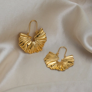 Gros plan de boucles d'oreilles dorées en forme d'éventail sur fond de soie beige