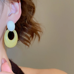 Close-up of model wearing oval acrylic earrings in cream white and olive green