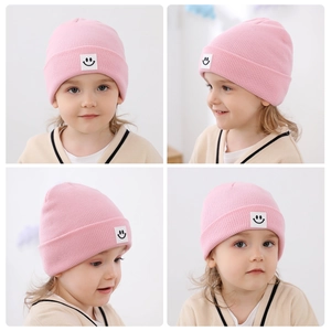 Dettaglio del berretto rosa in maglia con trama a coste e toppa con faccina sorridente