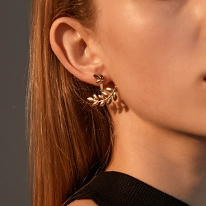 Close-up of golden olive leaf earrings on model under warm sunset lighting effects