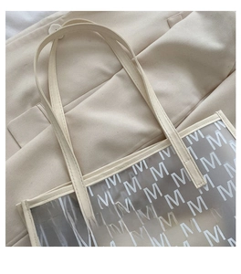 Detail of cream tote bag featuring monogram pattern and premium textured finish