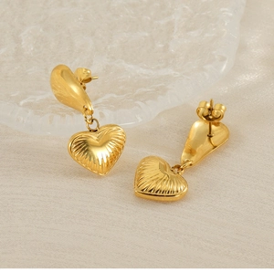 Detail view of gold heart drop earrings with radial texture on a glass tray