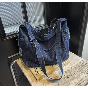 Gros plan du sac bandoulière en denim bleu foncé vintage avec bords effilochés sur marbre