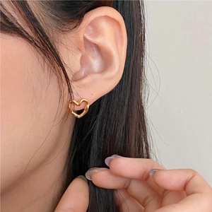 Close-up of golden hollow heart stud earrings with unique twisted texture on ear