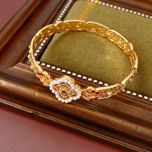 Detail of vintage gold-brushed bangle featuring carved flower with pearl and ruby inlay
