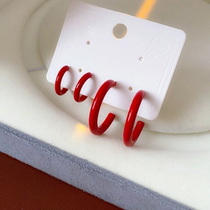Detailed close-up of four red C-shaped hoop earrings displayed on a white jewelry card